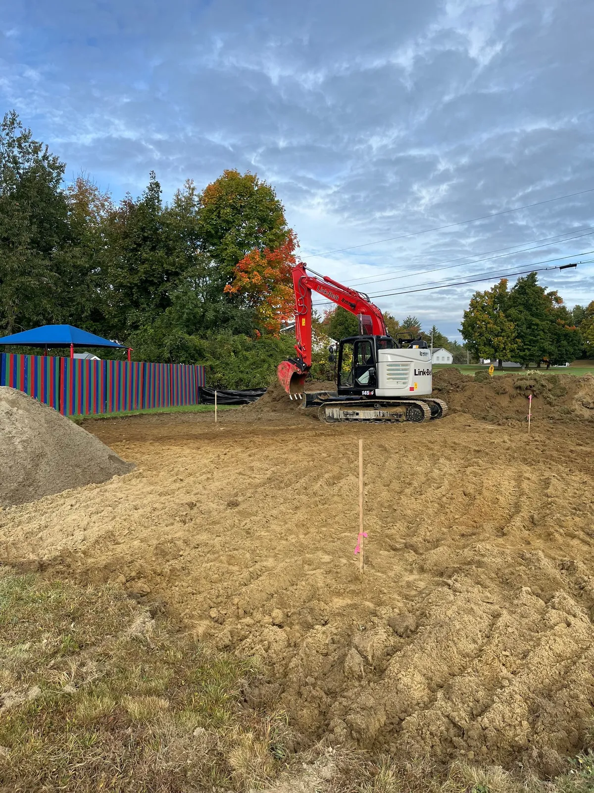 A red excavator working a dirt site under a cloudy sky.