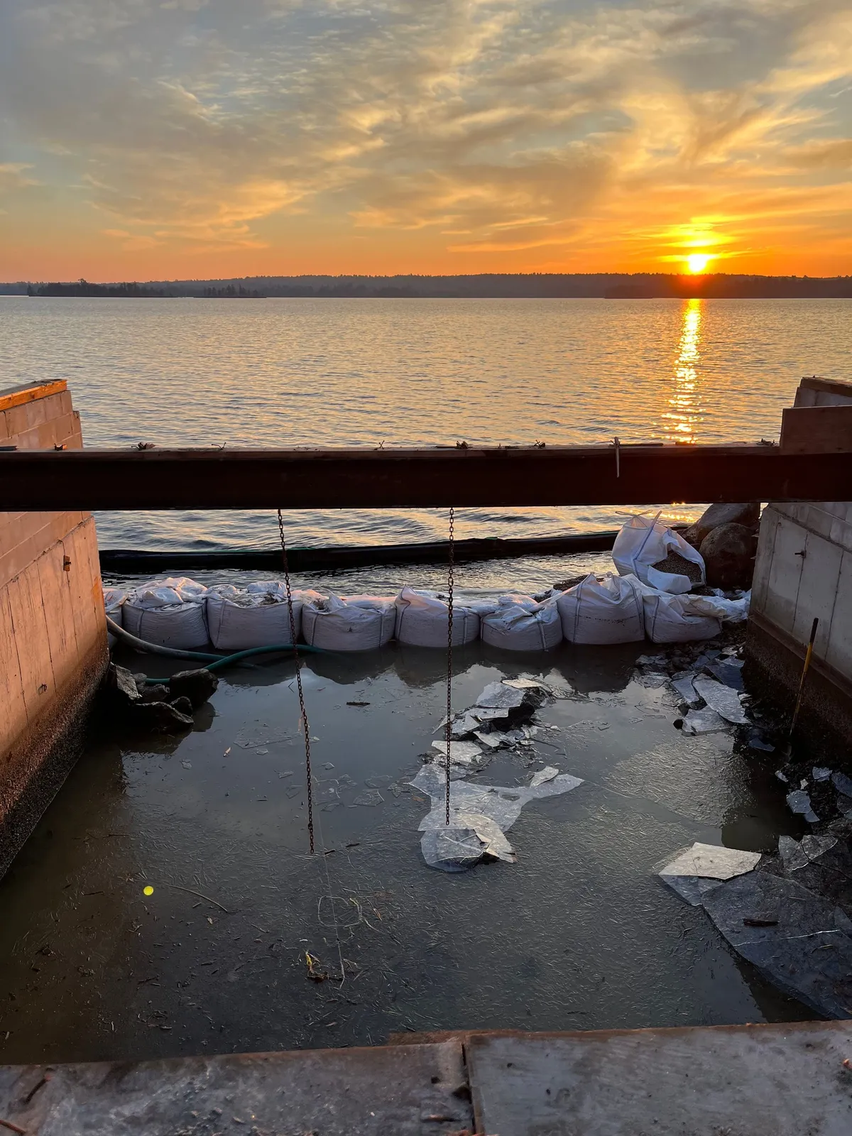 Sunset over the water past a line of white sandbags placed along a bank being stabilized.